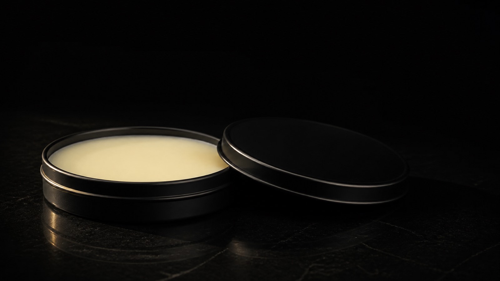 Beard Butter — seen in three-quarter view, low in a wide frame — under a single warm gold light on black.