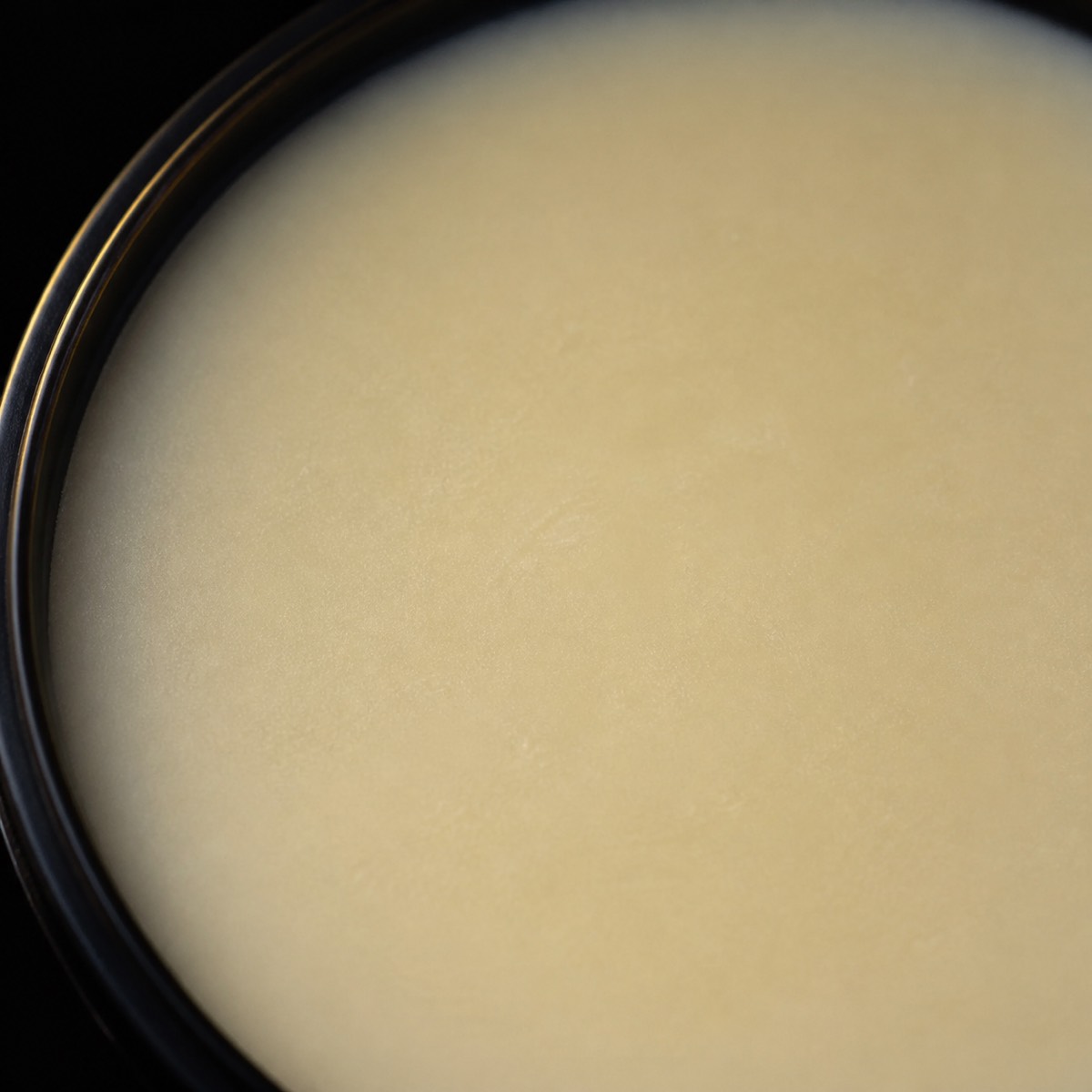 Beard Butter — the working end at magnification — under a single warm gold light on black.