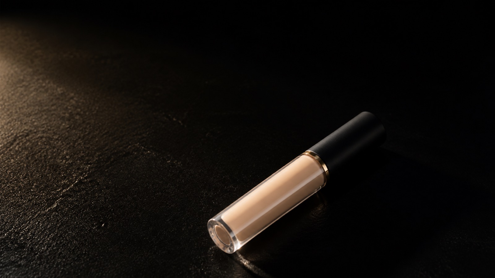Concealing Cream — seen in three-quarter view, low in a wide frame — under a single warm gold light on black.