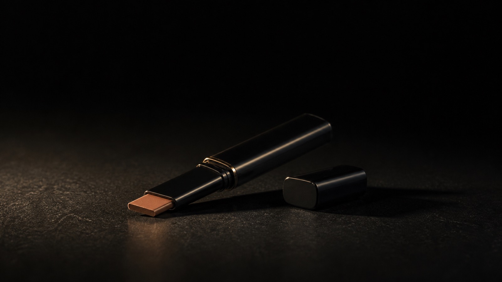 Concealer Stick — seen in three-quarter view, low in a wide frame — under a single warm gold light on black.