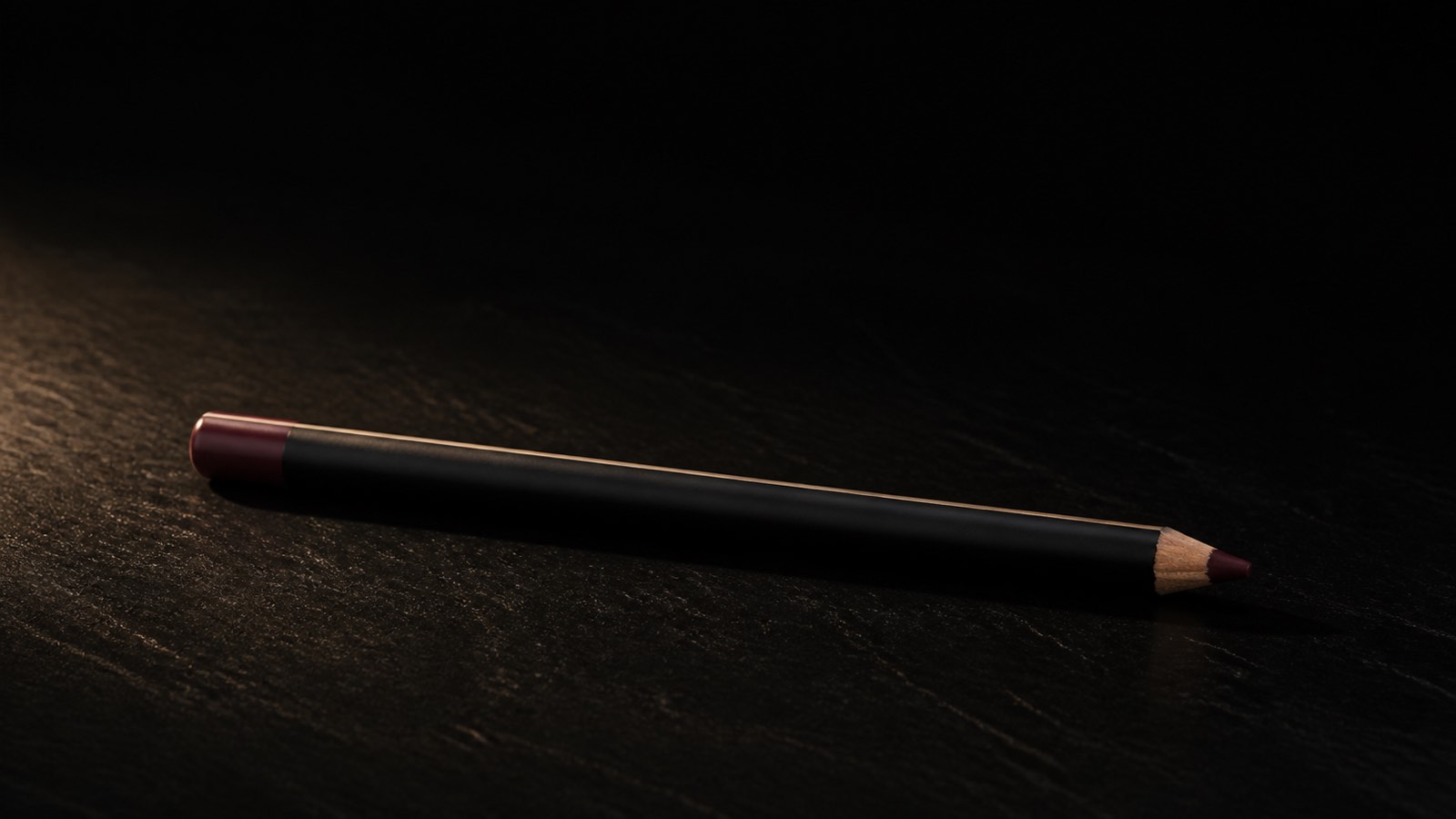 Lip Liner — seen in three-quarter view, low in a wide frame — under a single warm gold light on black.