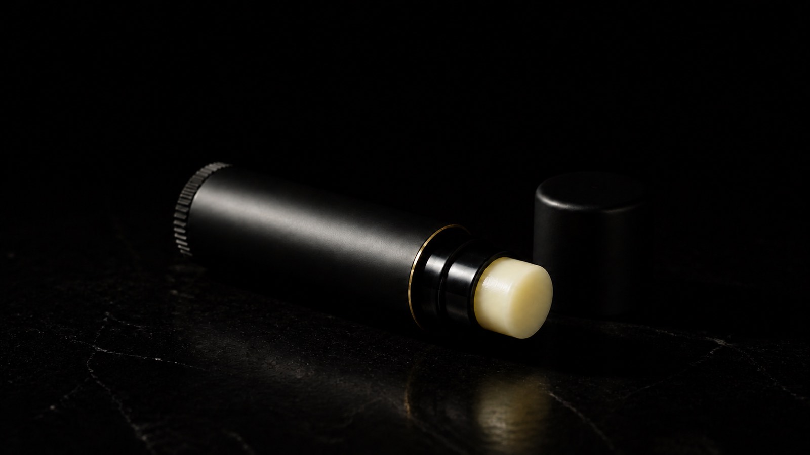 Vegan Lip Balm — seen in three-quarter view, low in a wide frame — under a single warm gold light on black.