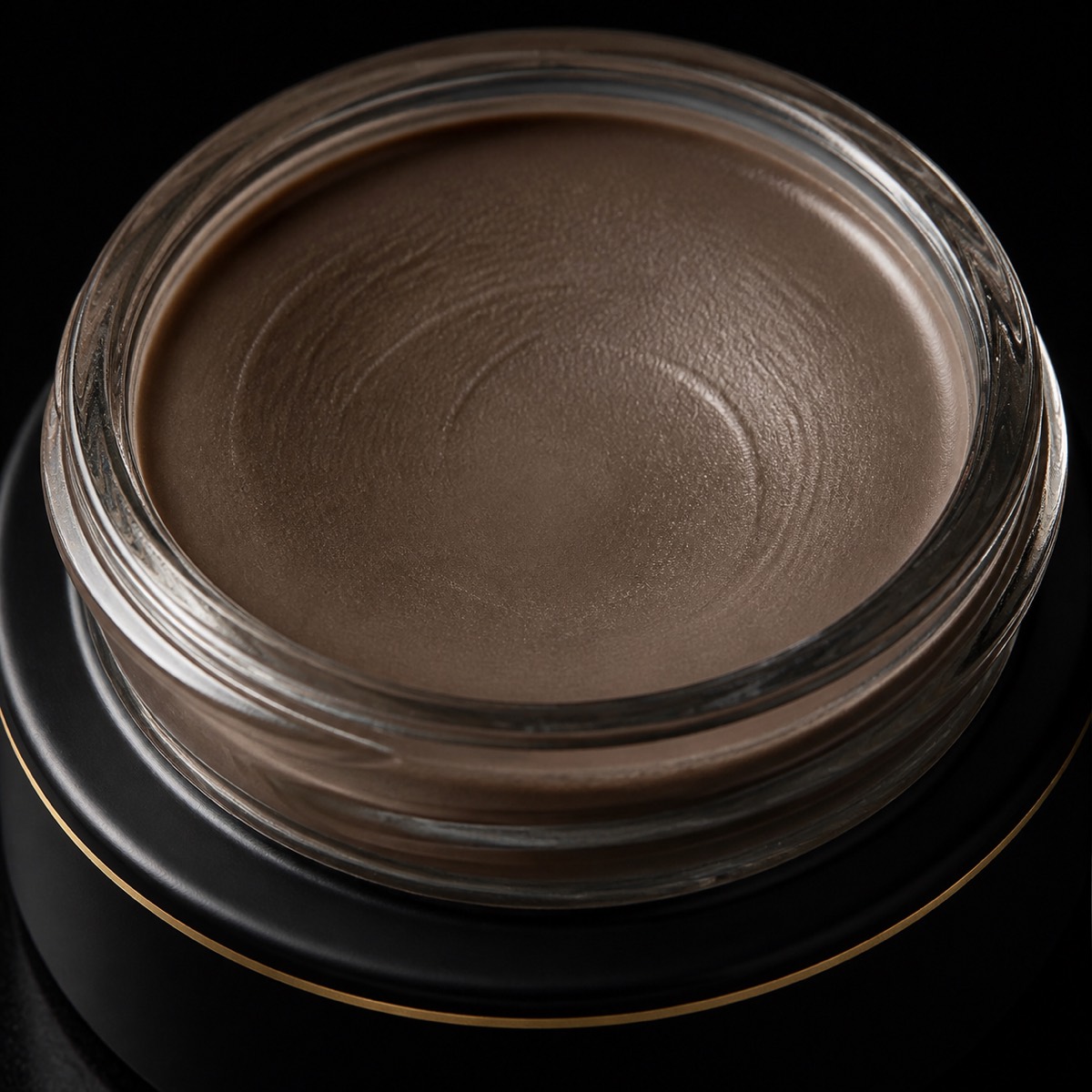 Brow Pomade — the working end at magnification — under a single warm gold light on black.