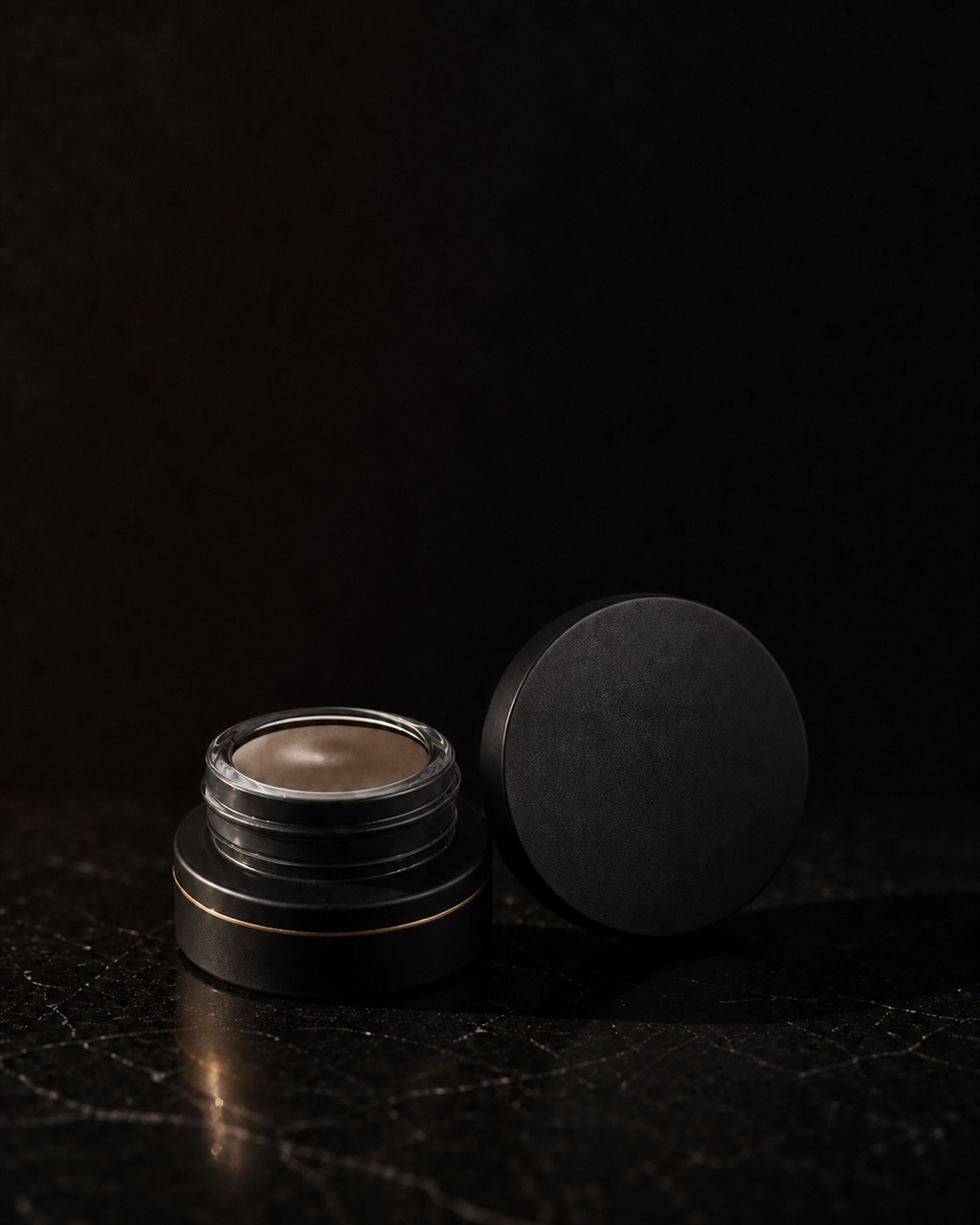 Brow Pomade — buildable brow color — standing alone against near-black under a single warm gold light.