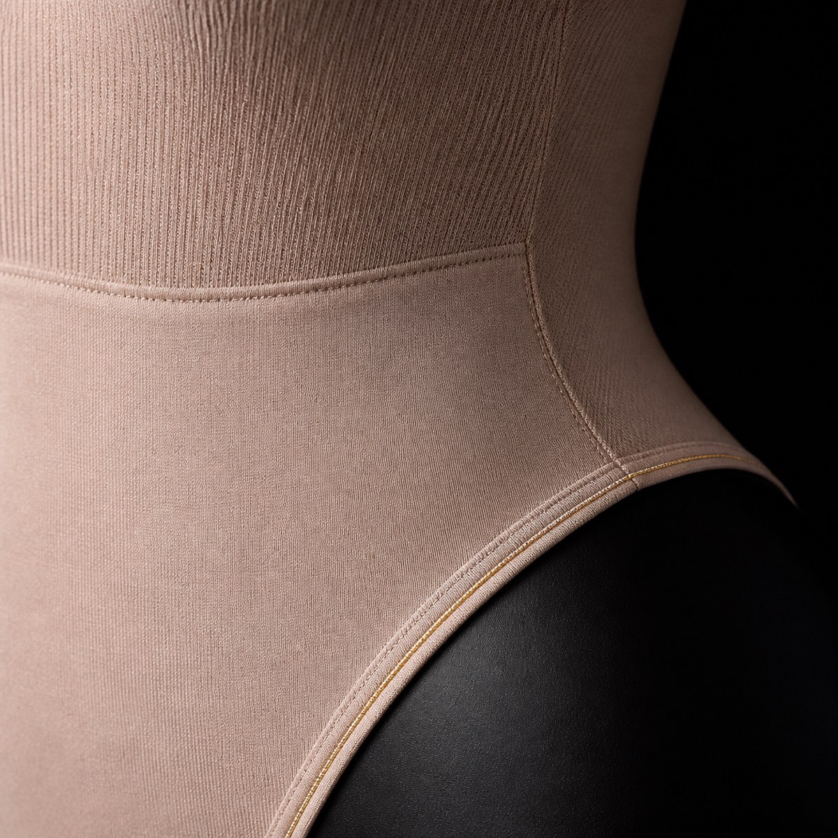 Scoop-Neck Shaping Bodysuit — the working end at magnification — under a single warm gold light on black.