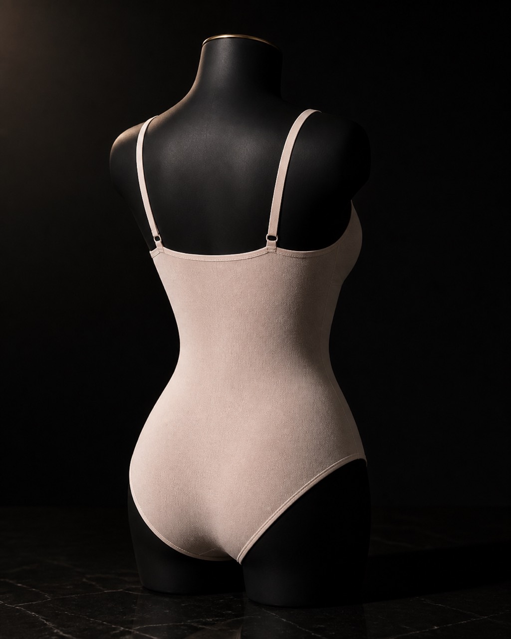 Scoop-Neck Shaping Bodysuit — open, arranged as it is used — under a single warm gold light on black.