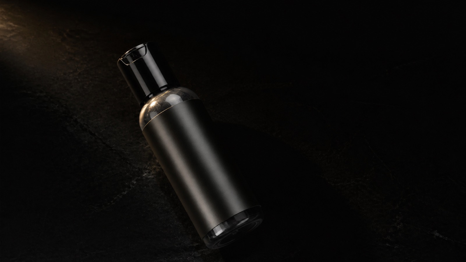 Charcoal Facial Cleanser — seen in three-quarter view, low in a wide frame — under a single warm gold light on black.