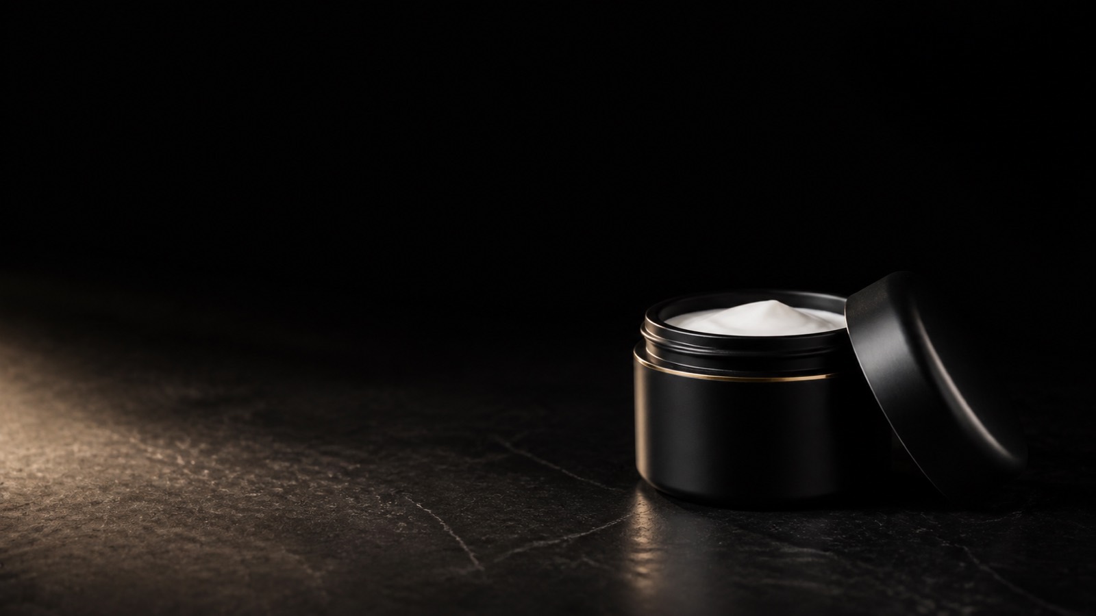 Skin Hydration Cream — seen in three-quarter view, low in a wide frame — under a single warm gold light on black.