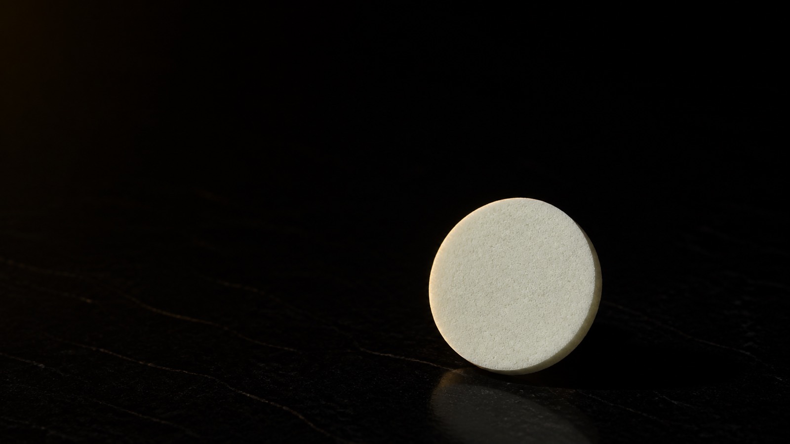 PVA Facial Sponge — seen in three-quarter view, low in a wide frame — under a single warm gold light on black.