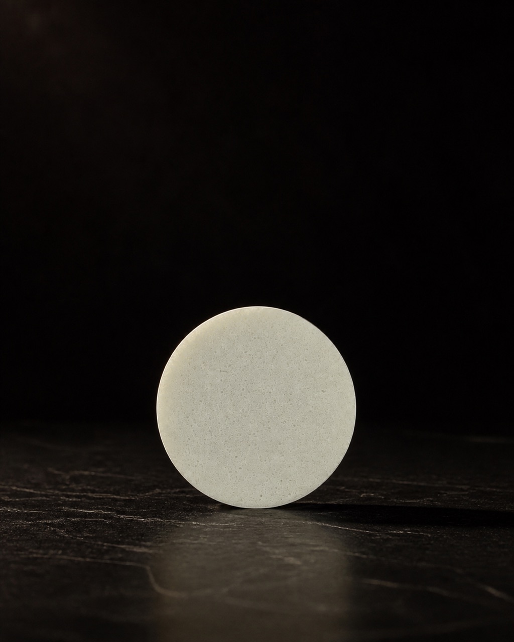 PVA Facial Sponge — washable facial sponge — standing alone against near-black under a single warm gold light.