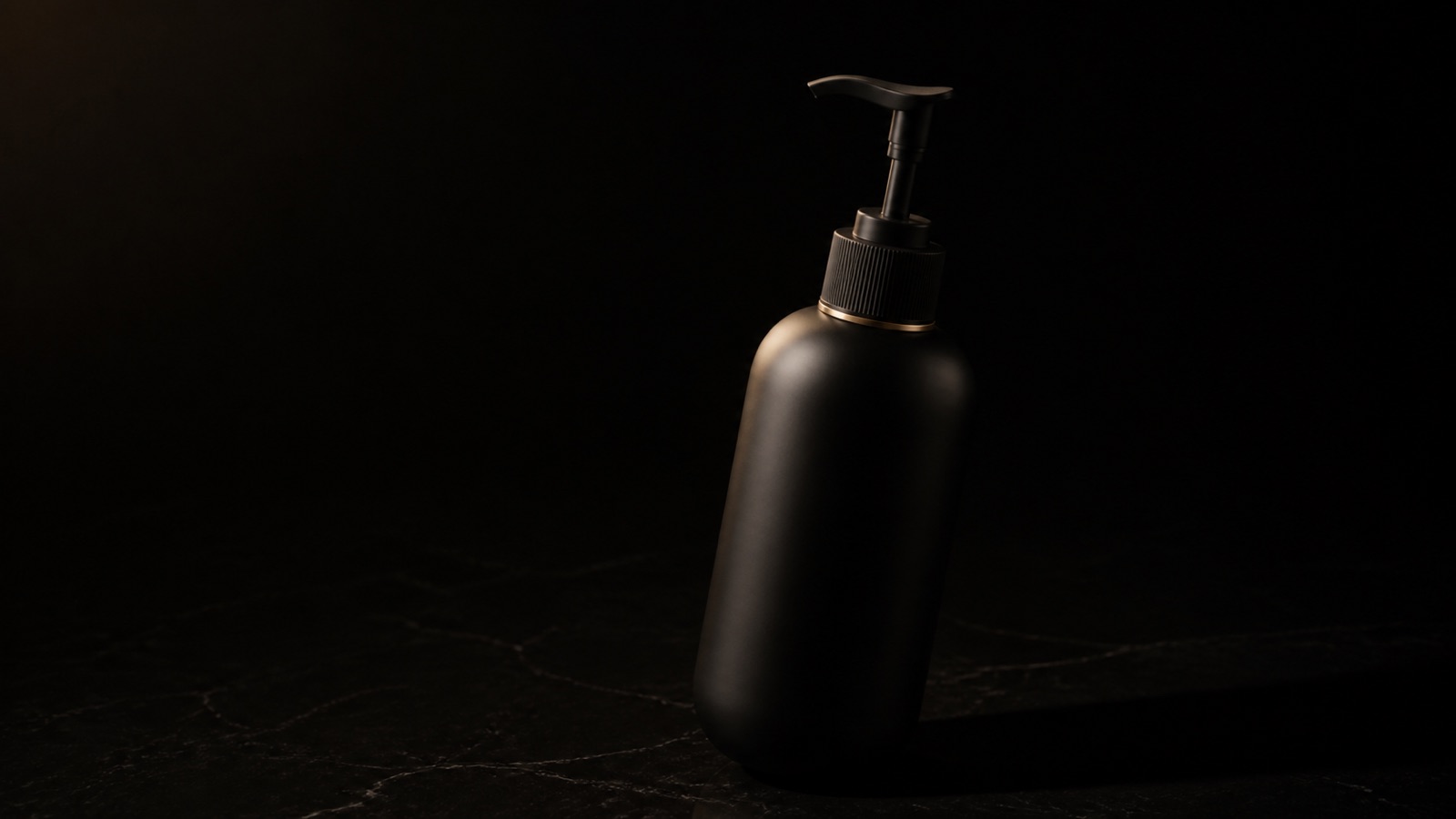 Hand & Body Moisturizer — seen in three-quarter view, low in a wide frame — under a single warm gold light on black.