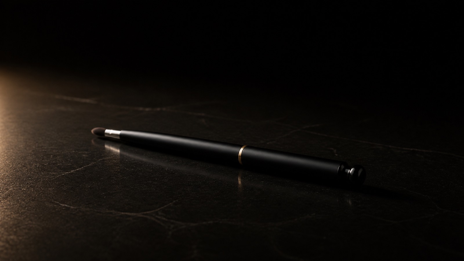 Retractable Lip Brush — seen in three-quarter view, low in a wide frame — under a single warm gold light on black.