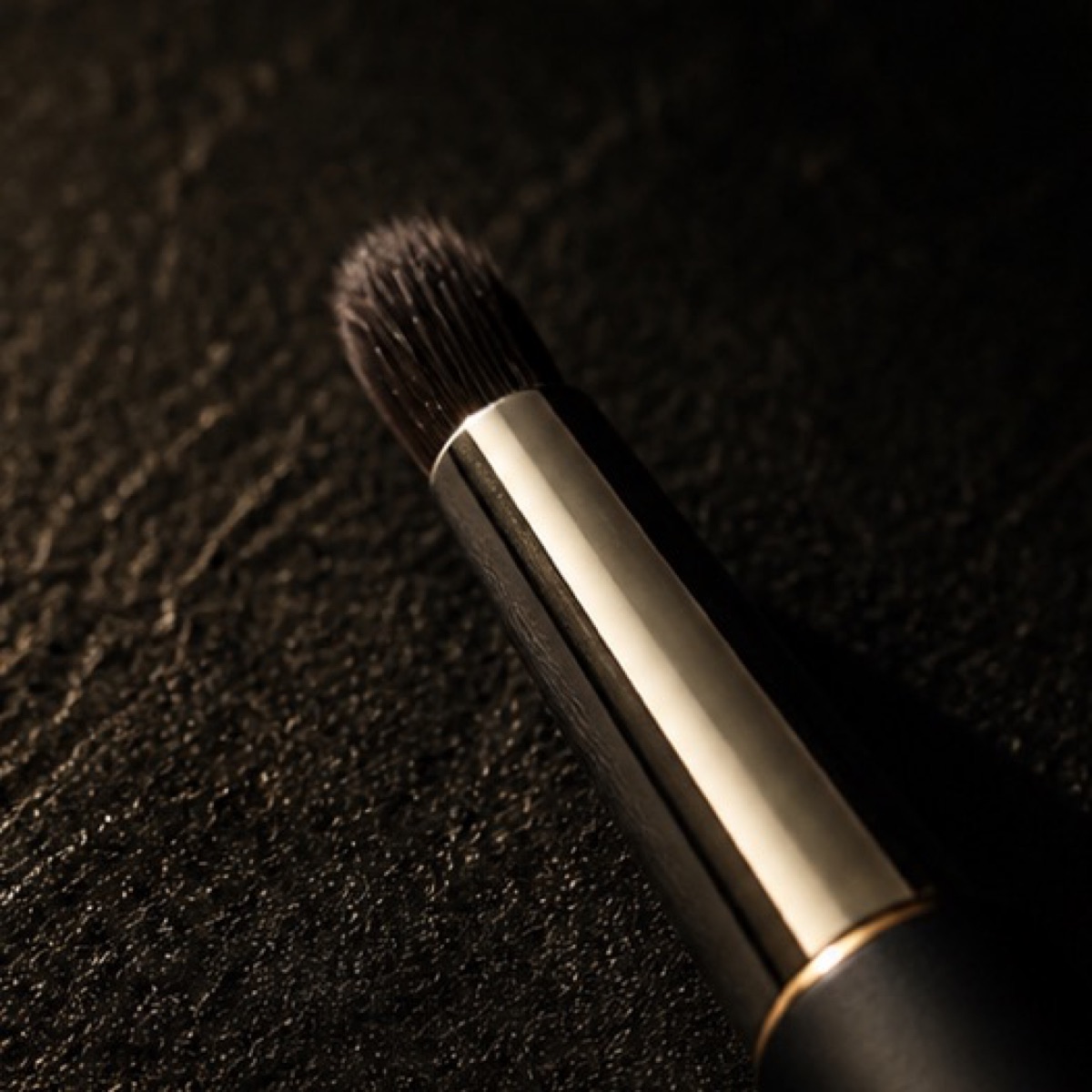 Retractable Lip Brush — the working end at magnification — under a single warm gold light on black.