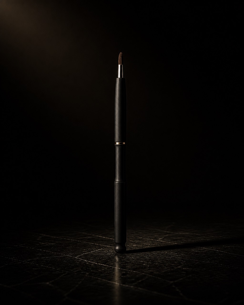 Retractable Lip Brush — retractable lip brush — standing alone against near-black under a single warm gold light.