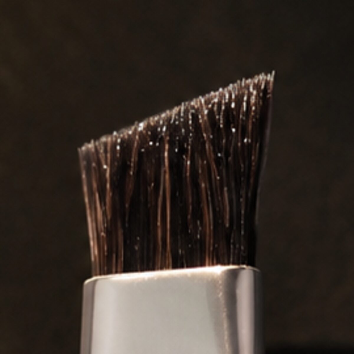 Brow Duo Brush — the working end at magnification — under a single warm gold light on black.