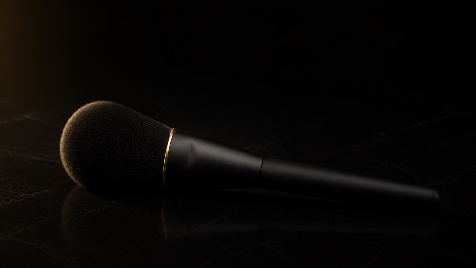 Tapered Powder Brush — seen in three-quarter view, low in a wide frame — under a single warm gold light on black.