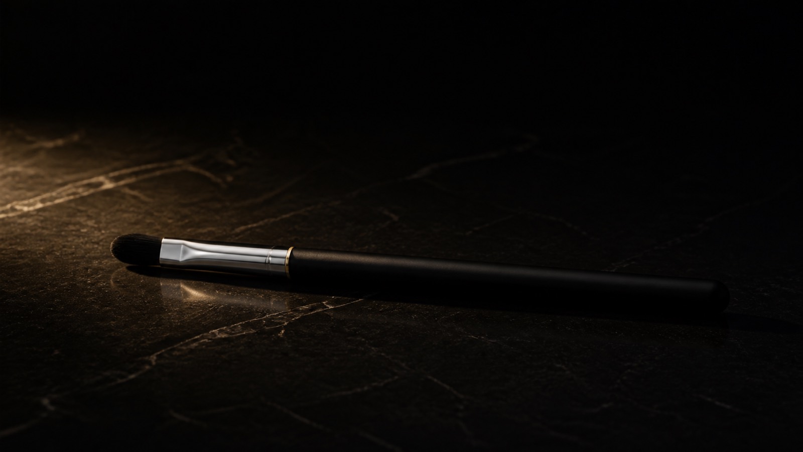 Oval Lip Brush — seen in three-quarter view, low in a wide frame — under a single warm gold light on black.