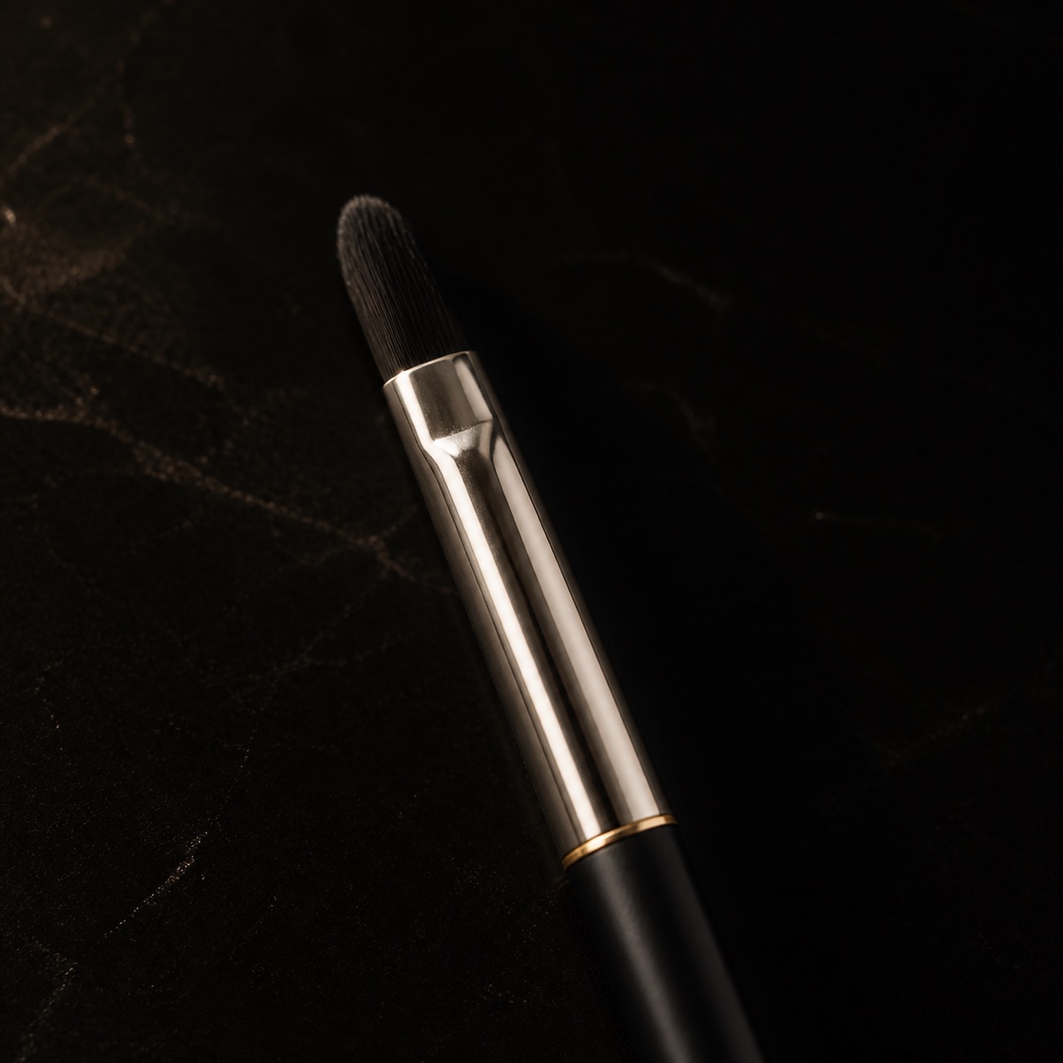 Oval Lip Brush — the working end at magnification — under a single warm gold light on black.