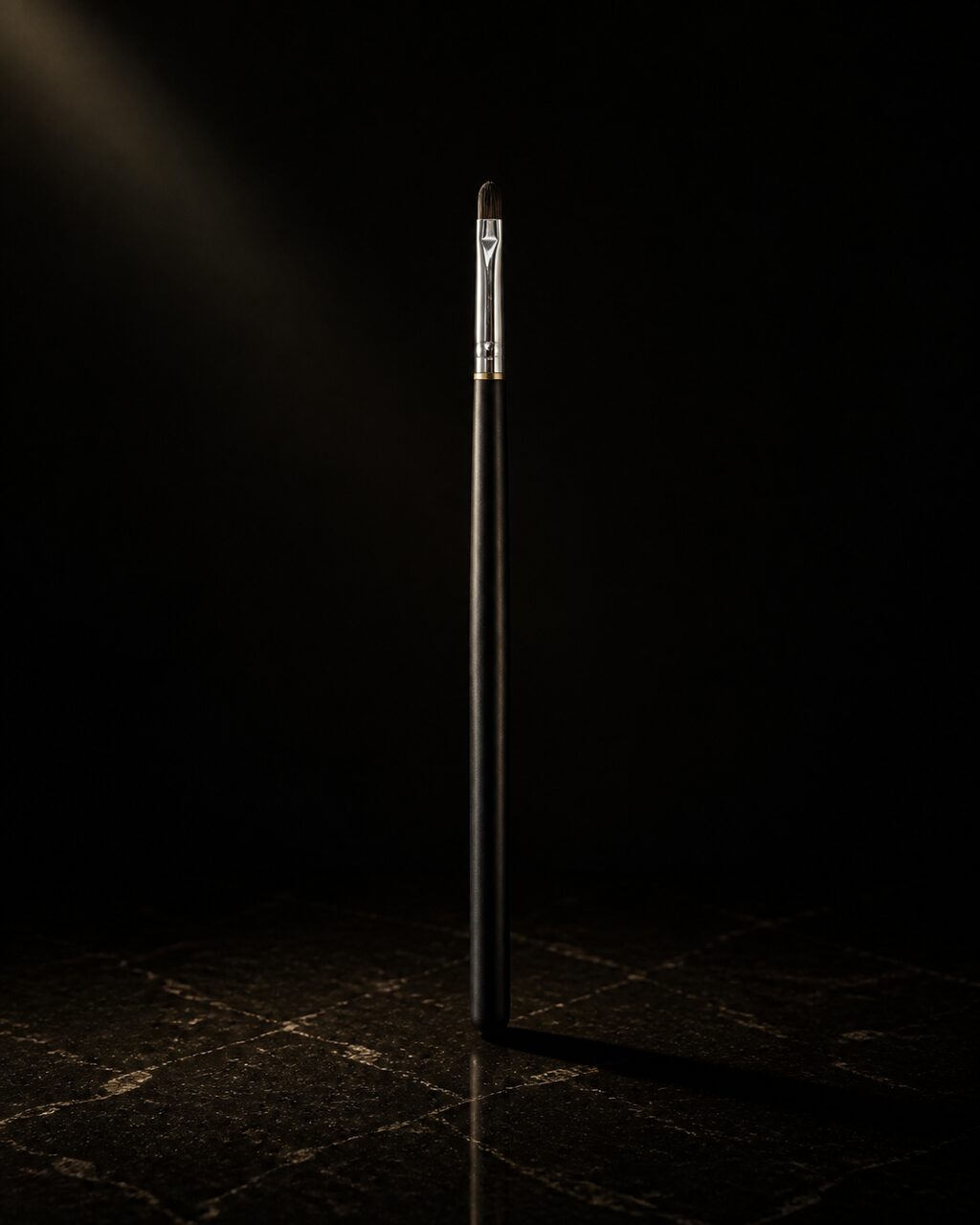 Pointed Lip Brush — pointed lip brush — standing alone against near-black under a single warm gold light.