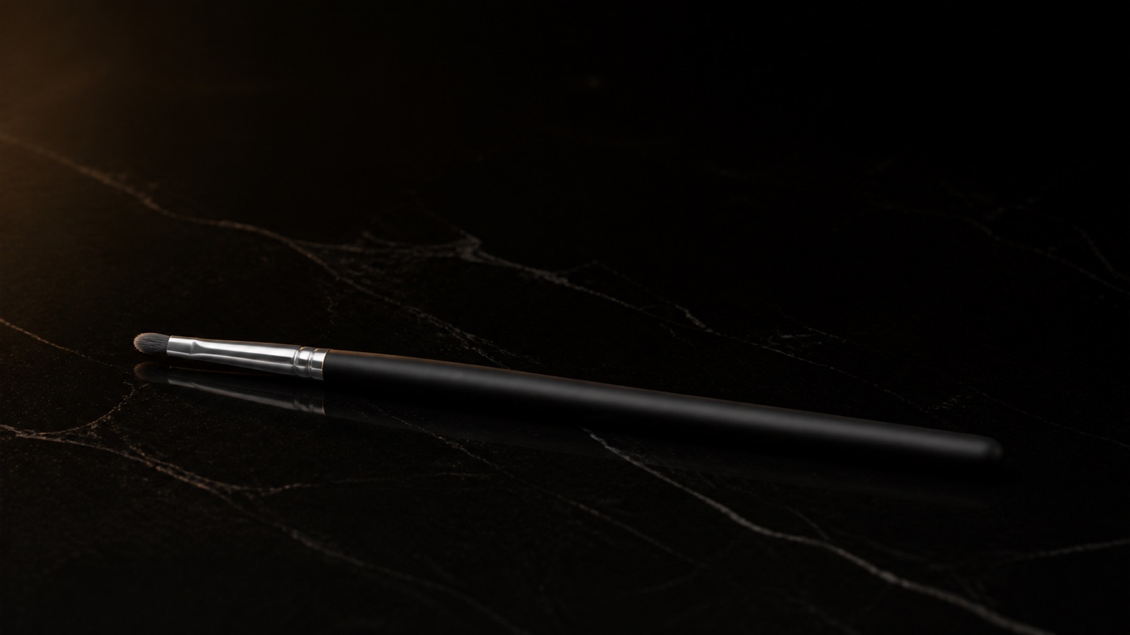 Small Detail Brush — seen in three-quarter view, low in a wide frame — under a single warm gold light on black.