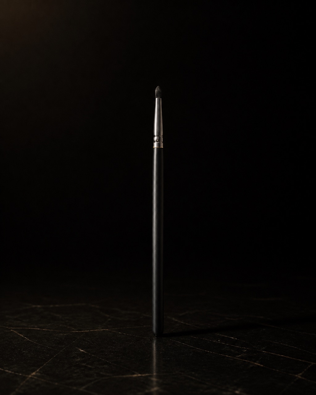 Small Detail Brush — precision detail brush — standing alone against near-black under a single warm gold light.