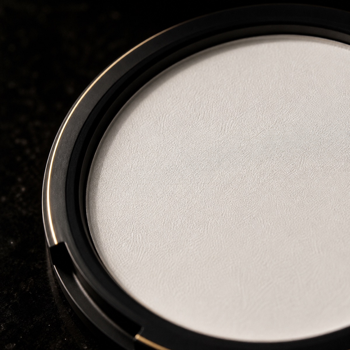 Translucent Pressed Powder — the working end at magnification — under a single warm gold light on black.