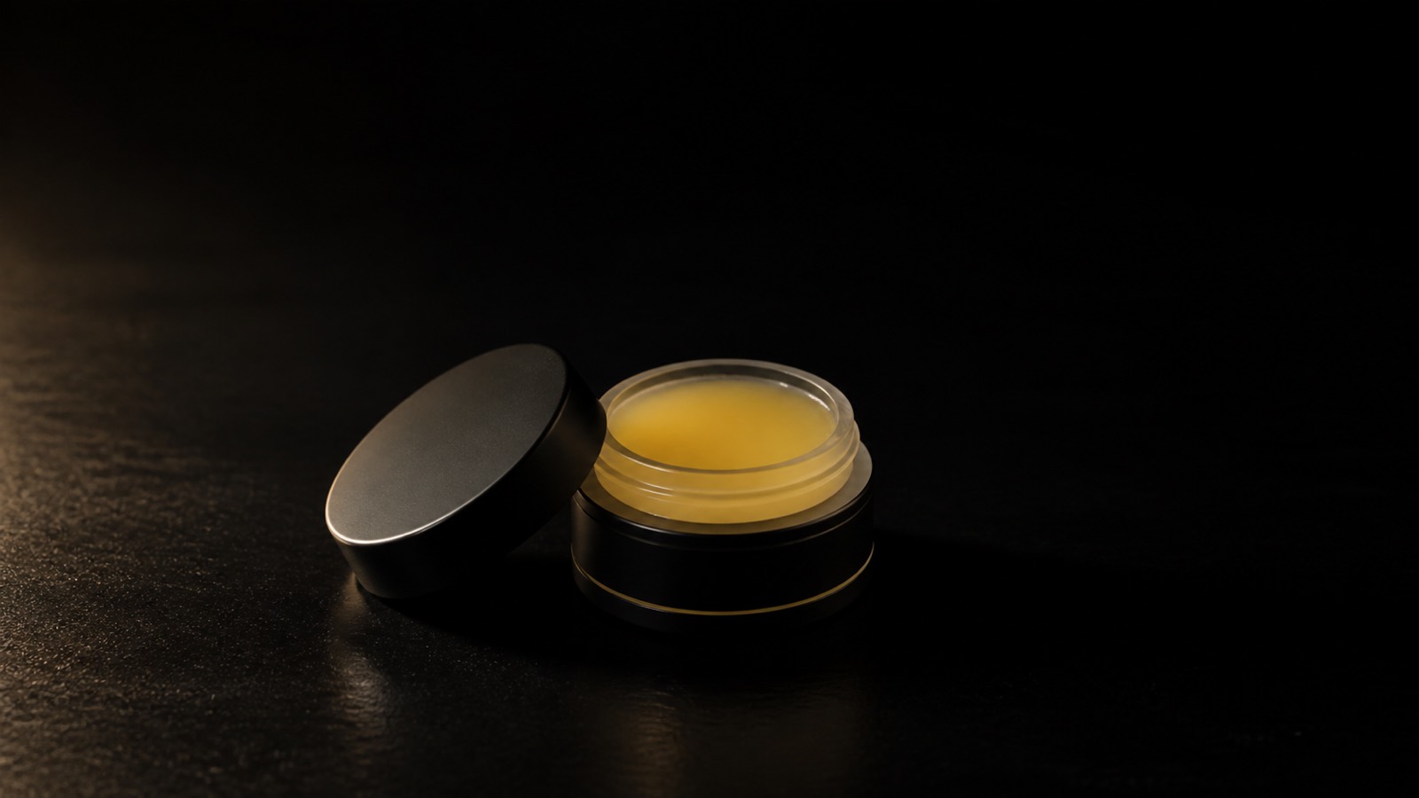 Lip Conditioner — seen in three-quarter view, low in a wide frame — under a single warm gold light on black.