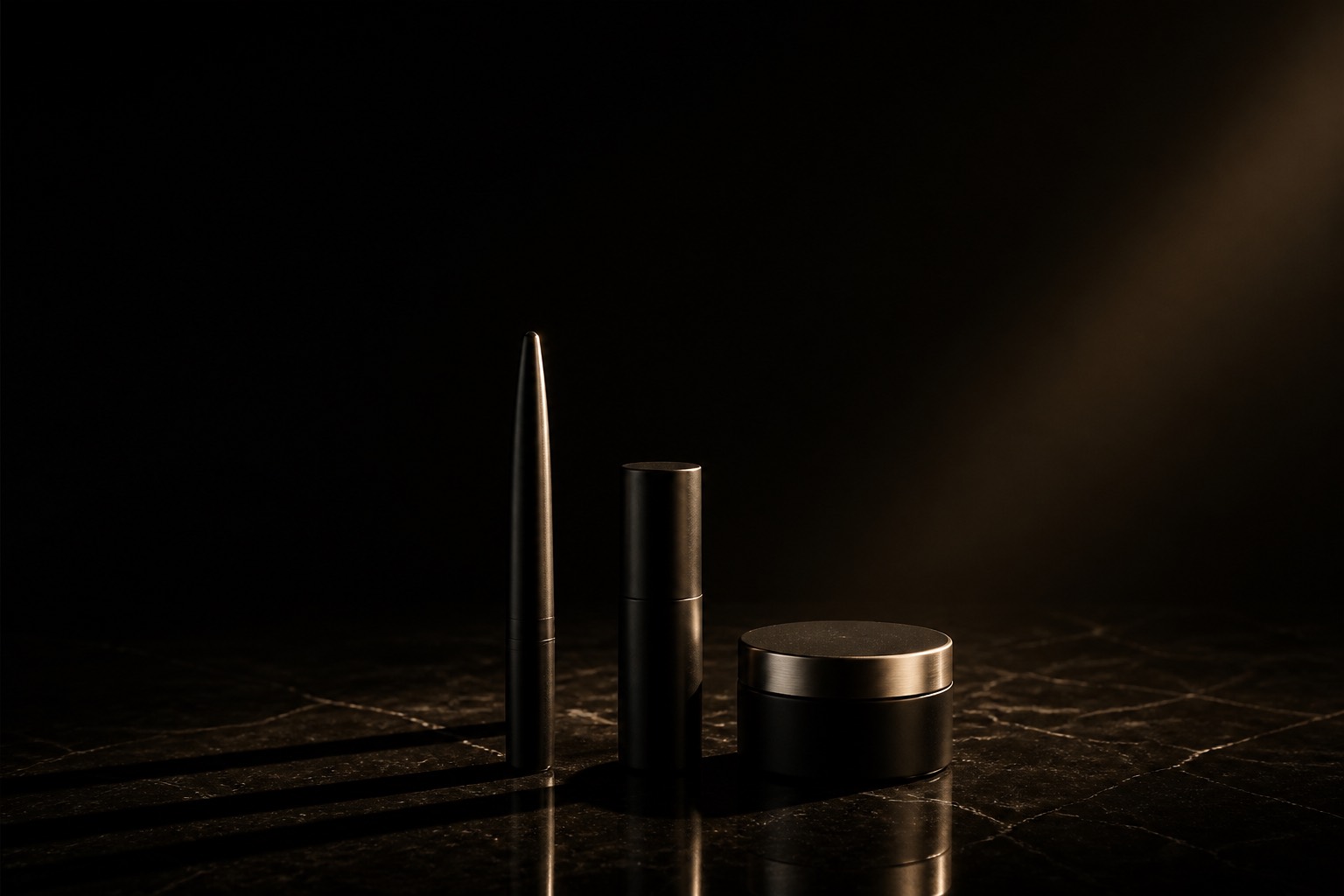 Three matte black objects arranged in near darkness under one warm light, long shadows to the right.