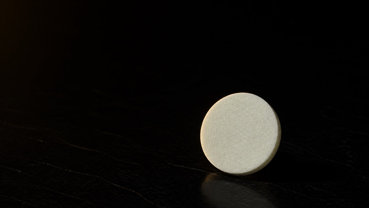 PVA Facial Sponge — seen in three-quarter view, low in a wide frame — under a single warm gold light on black.