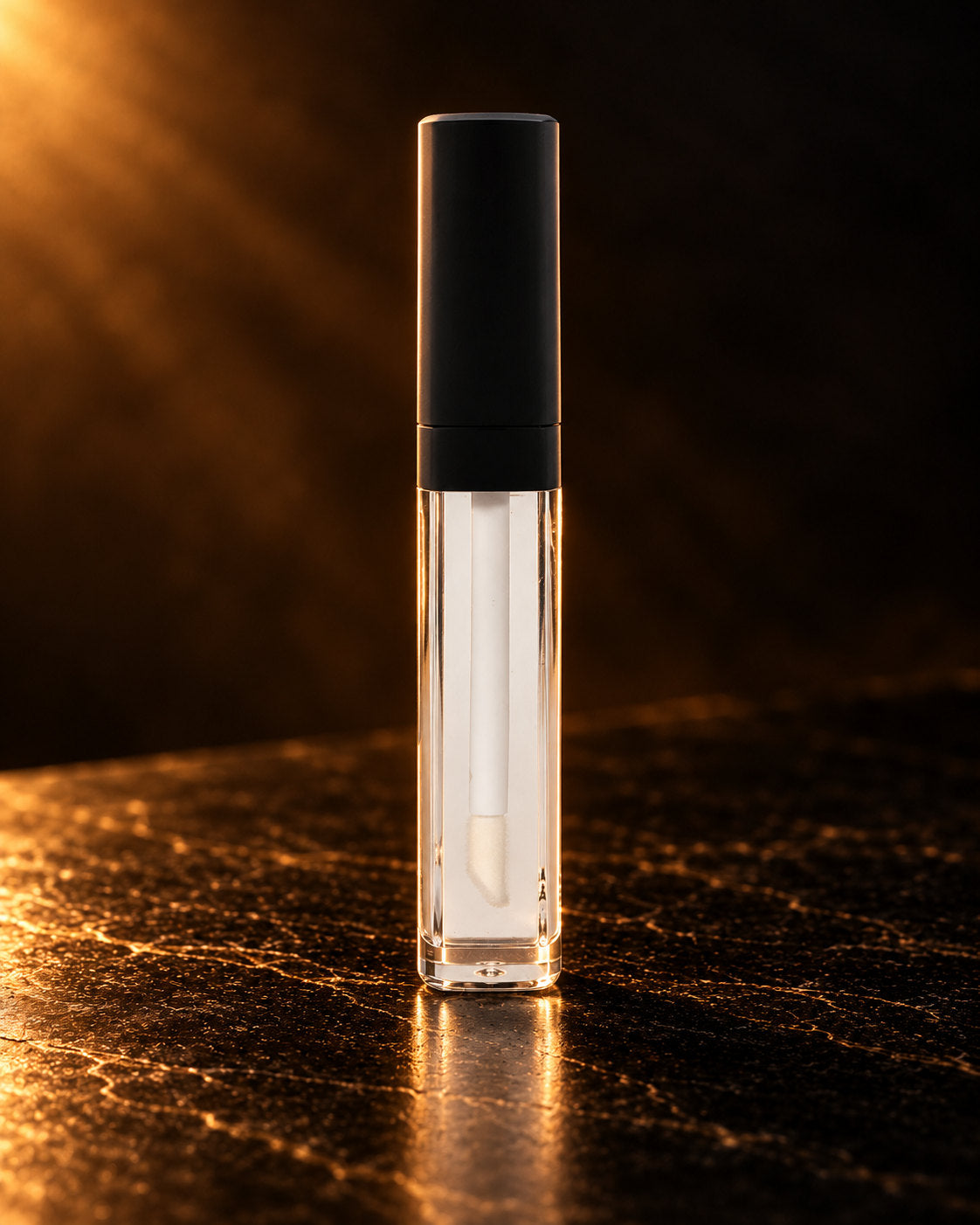 Clear Gloss in its square clear tube with a black cap, standing on dark stone in warm side light. Digitally styled image.
