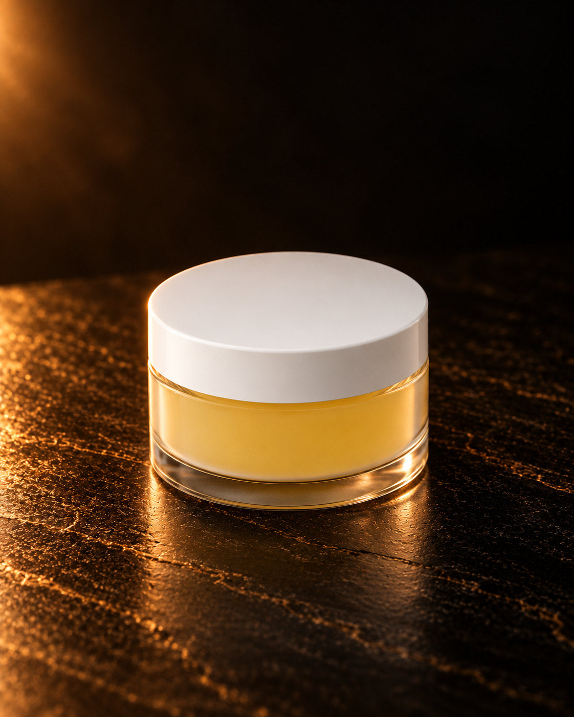 Lip Conditioner in Banana: pale yellow balm in a clear jar with a white lid, on dark stone in warm side light. Digitally styled image.