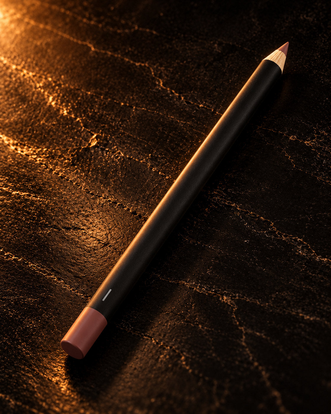 Lip Pencil in Be in Love 0054, a black pencil with a rose-brown tip, lying on dark stone in warm side light. Digitally styled image.
